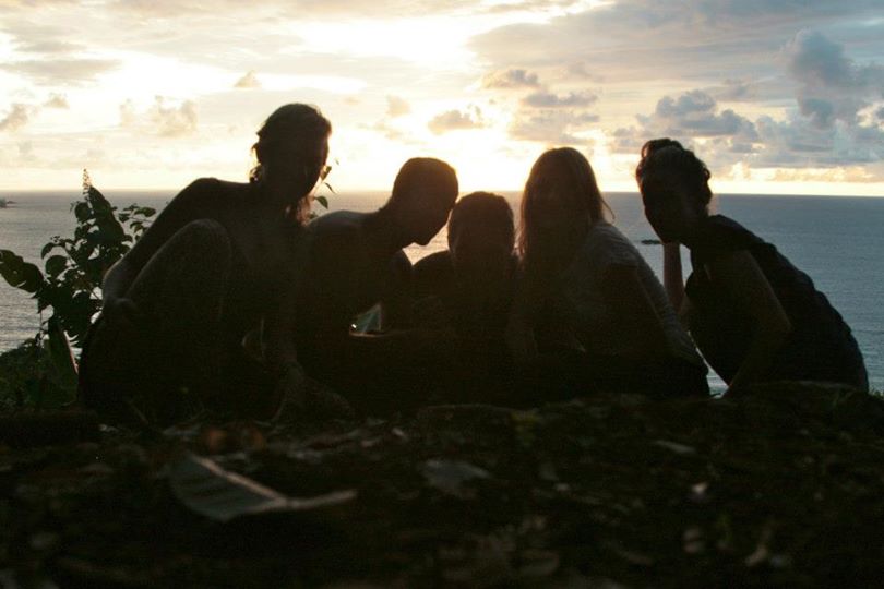 people on top of a hill with light of the sunset behind them and the wide ocean with a small island in the distance